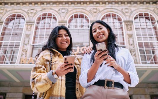 Front view of two Latina friends in city together looking at camera